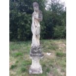 A composition stone garden statue cast as a draped lady covering her modesty on square plinth,