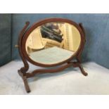 An oval Edwardian mahogany dressing table mirror, the bevelled plate on shaped supports with