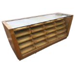 A haberdashery cabinet, the tapering counter with plate glass top and front enclosing twenty display