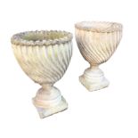 A pair of spirally moulded composition stone urns with serrated rims on circular socles and square