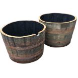 A pair of oak barrel garden planters, each with staves bound by three metal riveted strap bands. (
