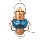 A copper ships hanging lantern gimbal swing mounts and cage framing blue-glass shade, surmounted
