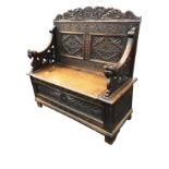 A Victorian carved oak settle with leaf scrolled back above a pair of lozenge foliate scrolled