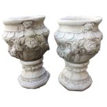 A pair of composition stone garden urns, the pots deeply moulded with flowers and leaves, incised to