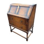An oak bureau with panelled fallfront revealing a fitted interior with small drawer, the desk with