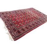 An Afghan carpet woven with madder field of hooked octagonal medallions and crosses, framed by