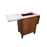 A mahogany sewing machine cabinet, the moulded top hinging in two halves revealing a recess for a