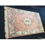 A Chinese thick pile wool rug woven with an oval floral medallion on pale pink ground, framed by