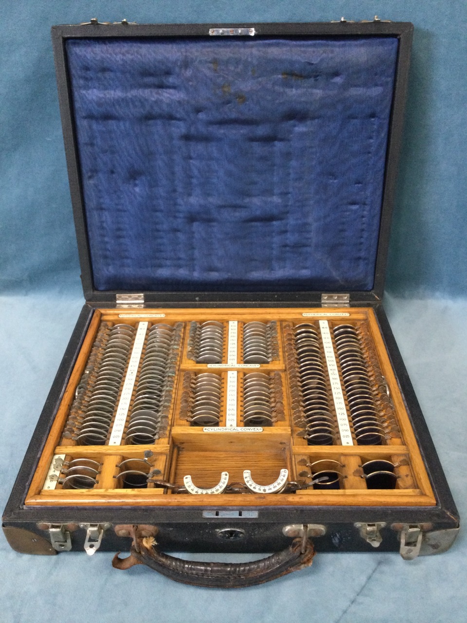 A cased optometrist set of glasses, the numbered lenses in fitted oak tray, the case with brass