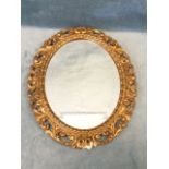 An antique bevelled mirror in oval frame with leaf moulded border, within a pierced scrolled