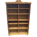 A pine open bookcase with arched carved crest above adjustable shelves, framed by fluted stiles,