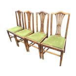 A set of four Edwardian oak dining chairs with arched backs and pierced splats, having drop-in