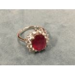 A large platinum ruby & diamond ring, the oval claw set stone of approx 8cts, framed by border of