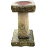 A composition stone garden birdbath with square basin on tapering chamfered column above a square