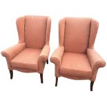 A pair of upholstered wing armchairs with padded backs and scroll shaped arms above sprung seats