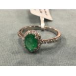 A platinum emerald & diamond ring, the oval claw set emerald of mint green colour framed by border