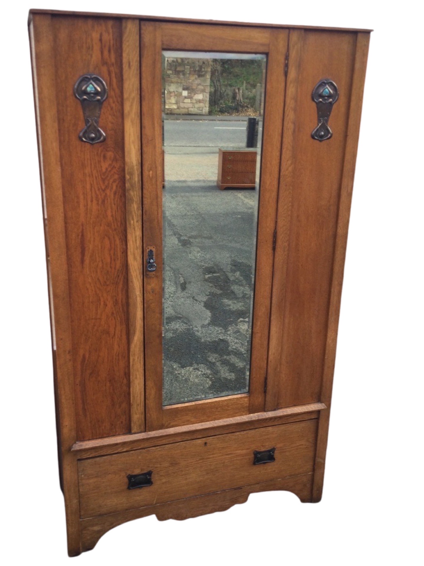 An art nouveau oak wardrobe with central bevelled mirror door framed by panels with applied anodised