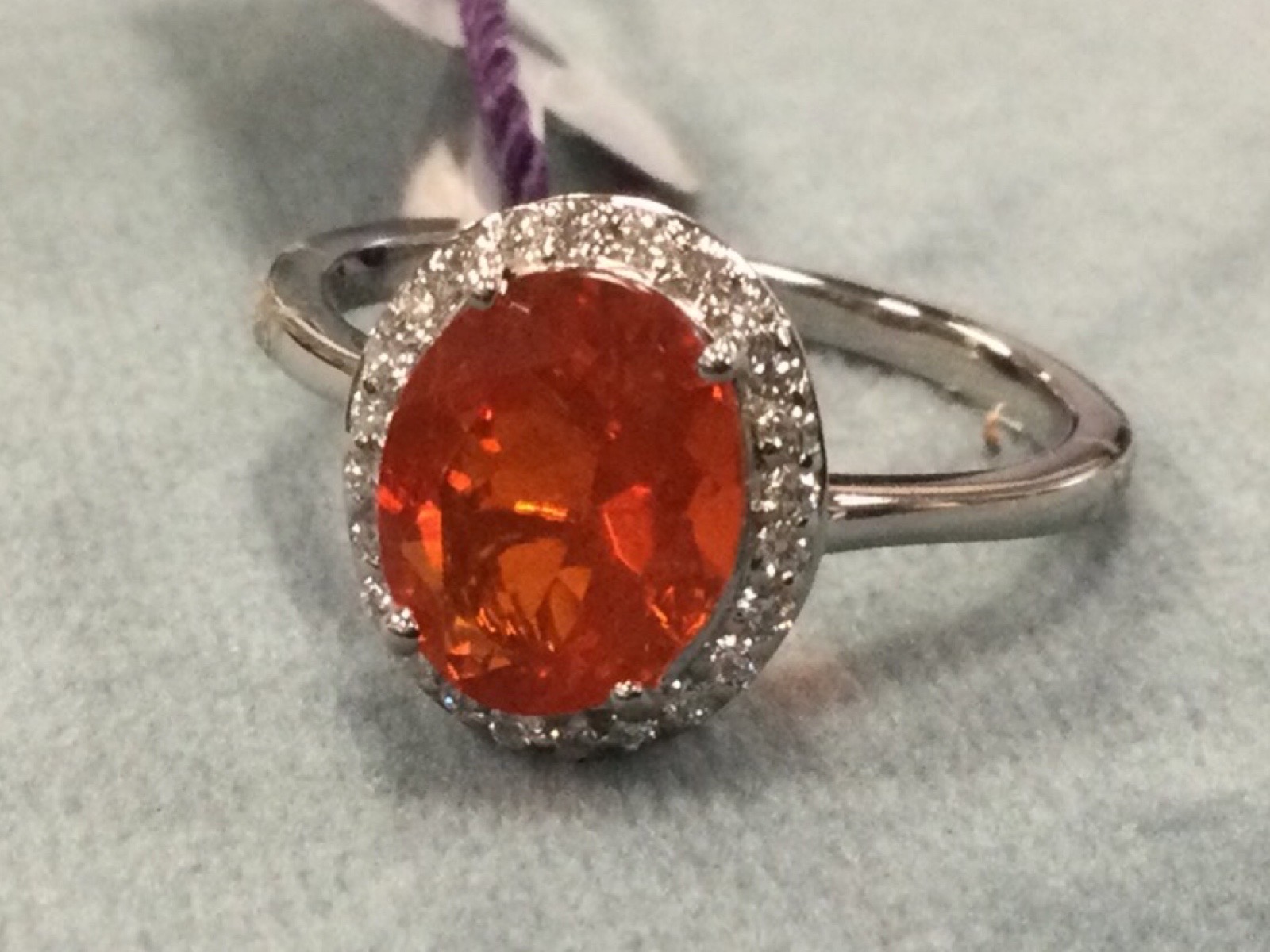 A platinum fire opal ring, the claw set oval Salamanca fire opal framed by border of small diamonds,