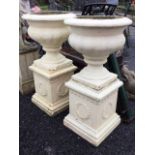 A pair of painted composition stone urns with cushion rims above fluted bodies with socles and