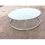 A contemporary circular coffee table with plate glass top on brushed chrome base, having two rings