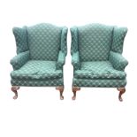 A pair of upholstered Georgian style wing-back armchairs, the wide sprung seats with loose cushions,
