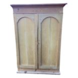 A Victorian pine wardrobe with angled cornice above arched panelled doors, the painted interior with