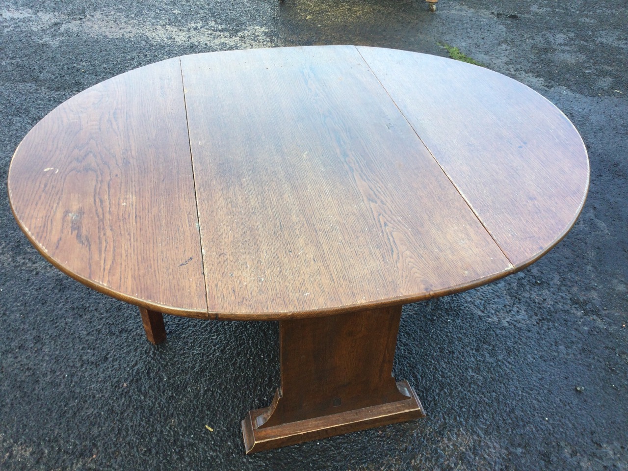 An oval oak coffee table with drop leaves on rectangular supports with batten feet, the gates with