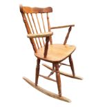 A pine rocking chair with spindle back and tapering platform arms, the solid seat raised on turned