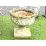 A circular composition stone garden urn with leaf moulded pot on squat column with square plinth. (