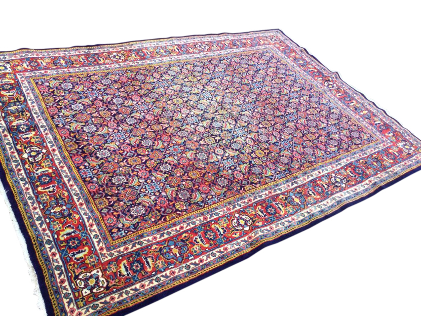 A Persian wool rug woven with multi-floral grid field on blue ground, framed by frieze of linked