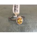 An 18ct white gold ring claw set with an oval yellow sapphire framed by border of small diamonds,