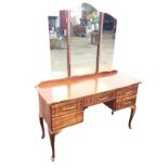 A 1960s walnut dressing table with three mirror plates above a shaped rectangular top, the rippled