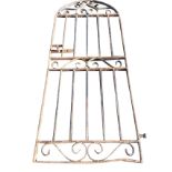 A heavy iron garden gate with arched top framing scrolled panel, having rectangular panels with