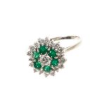 Emerald and diamond cluster ring with a central brilliant cut diamond surrounded by emeralds and a f