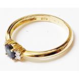 An import marked 750 gold ring, set with central small oval sapphire and four flanking tiny diamonds