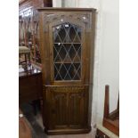 A 72cm modern oak freestanding corner cabinet with leaded glazed panel door to top over a linen fold