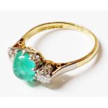 A hallmarked 18ct. gold and platinum ring, set with a central emerald cabochon and flanking diamonds