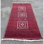 A modern handmade rug decorated with three square central panels and decorated border on a red and
