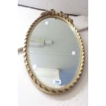 A vintage gilt framed bevelled oval wall mirror with bow and floral decoration to top