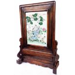 An antique Chinese hardwood table screen and carved stand, inset with a porcelain panel decorated in