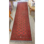 A handmade Middle Eastern runner with repeat medallion decoration and geometric border on red ground