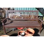 A teak three seater garden bench with slatted seat and back and brown stained finish
