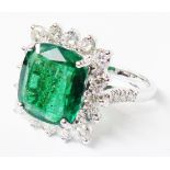 A marked 18k white metal ring, set with large central emerald within a sixteen stone brilliant cut