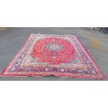 A handmade Persian wool carpet with repeat motifs on red ground within a wide triple border