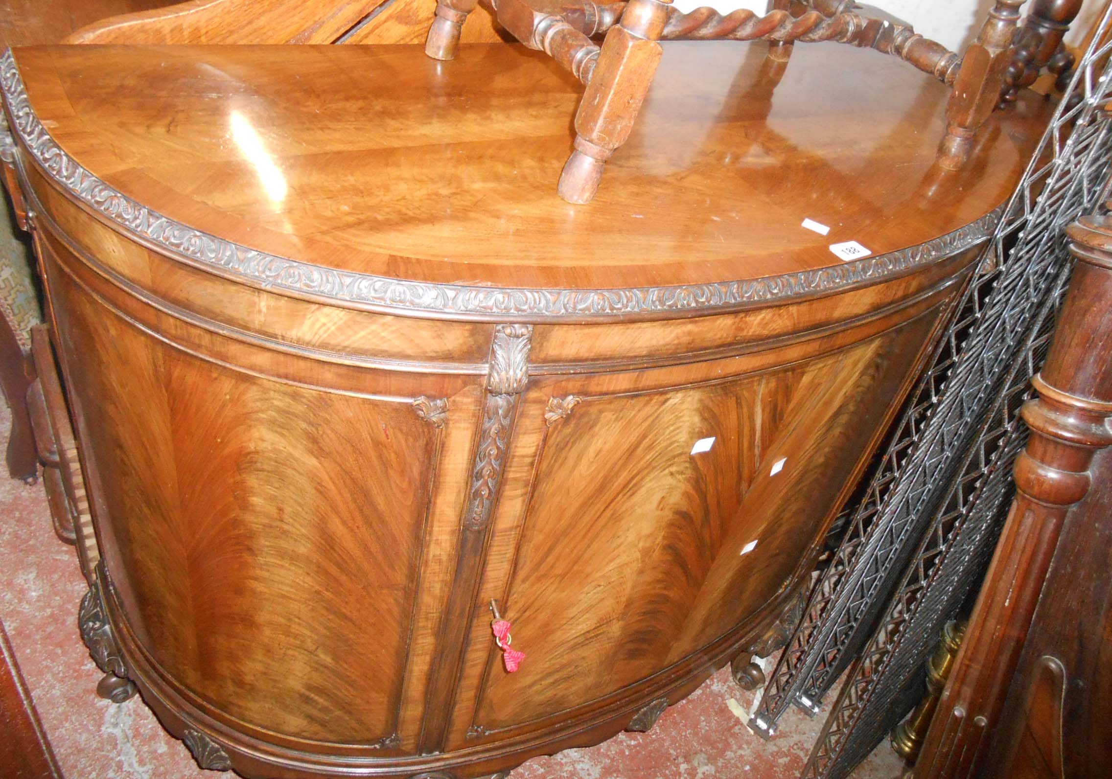 A 1.17m 1920's flame mahogany and crossbanded bow front sideboard with carved decoration and shelves