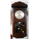 An early 20th Century stained oak cased wall clock with visible pendulum and eight day gong striking