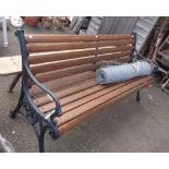 A wrought iron three seater garden bench with wooden slatted seat