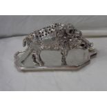 A silver plated boar pattern hat pin holder, standing on a modern silver two handled tray