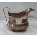 An antique silver cream jug with ribbed rim and handle - dents