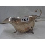 A silver gravy boat with cast scroll handle, set on paw pattern feet - dent